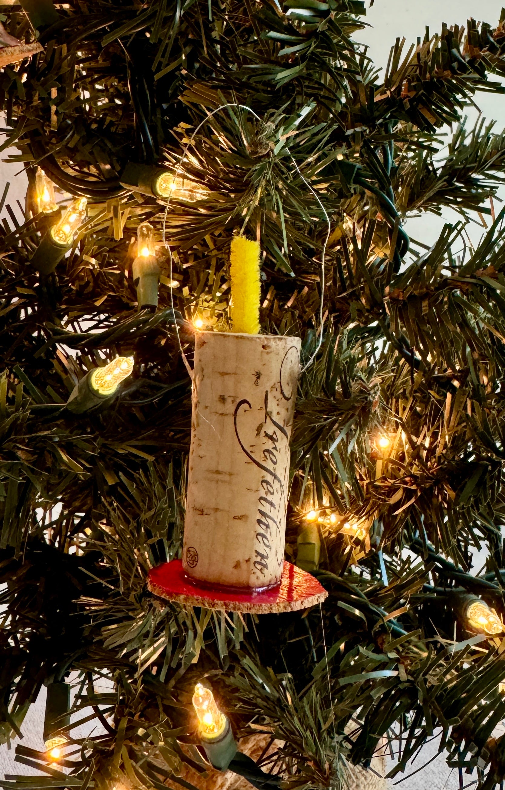 Close up of candle ornament made of wine cork and yellow pipe cleaner wick sitting on red base