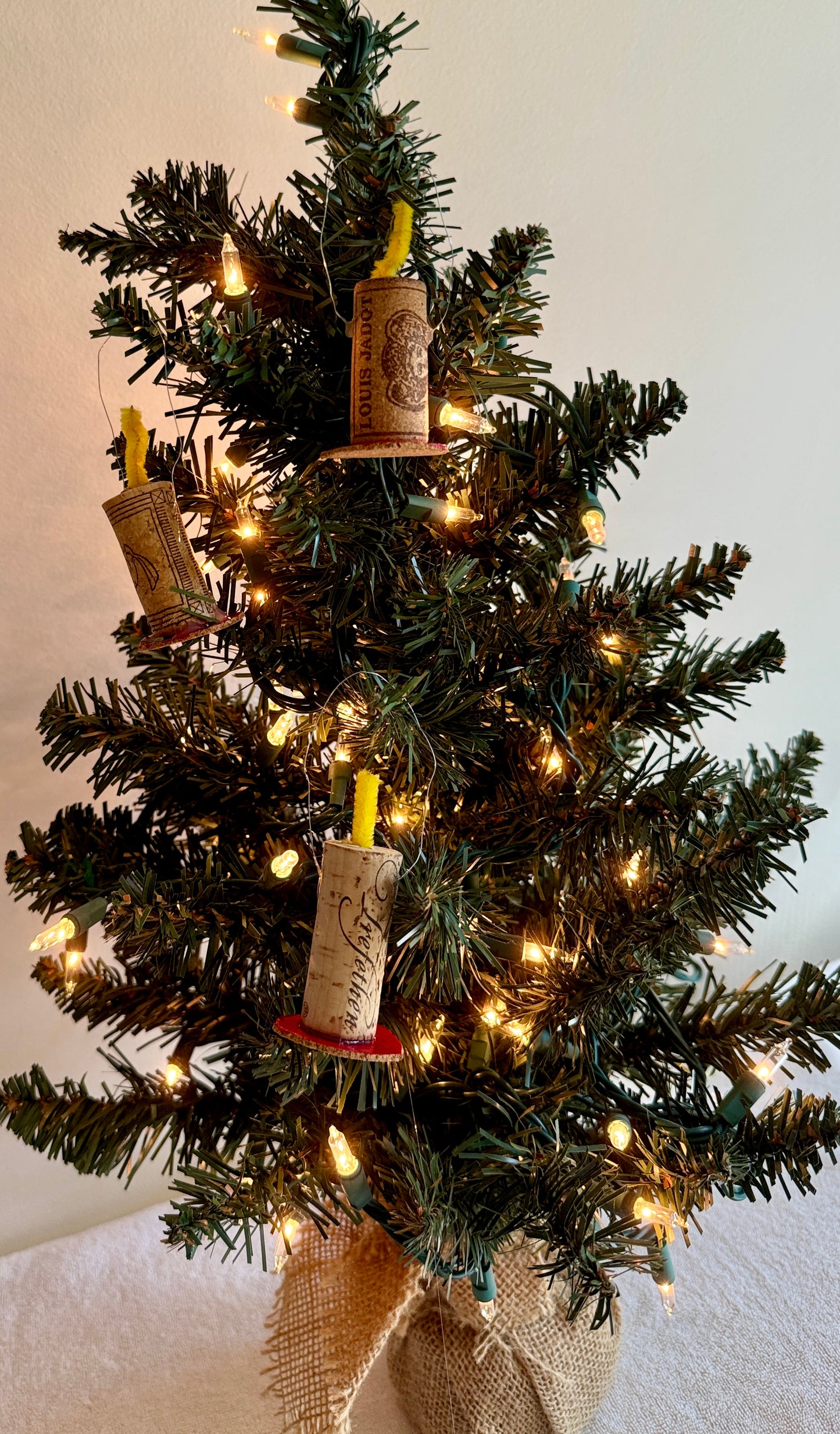 Wine corks made to look like Christmas candles with yellow pipe cleaner wick and sitting on red base, hanging Christmas tree