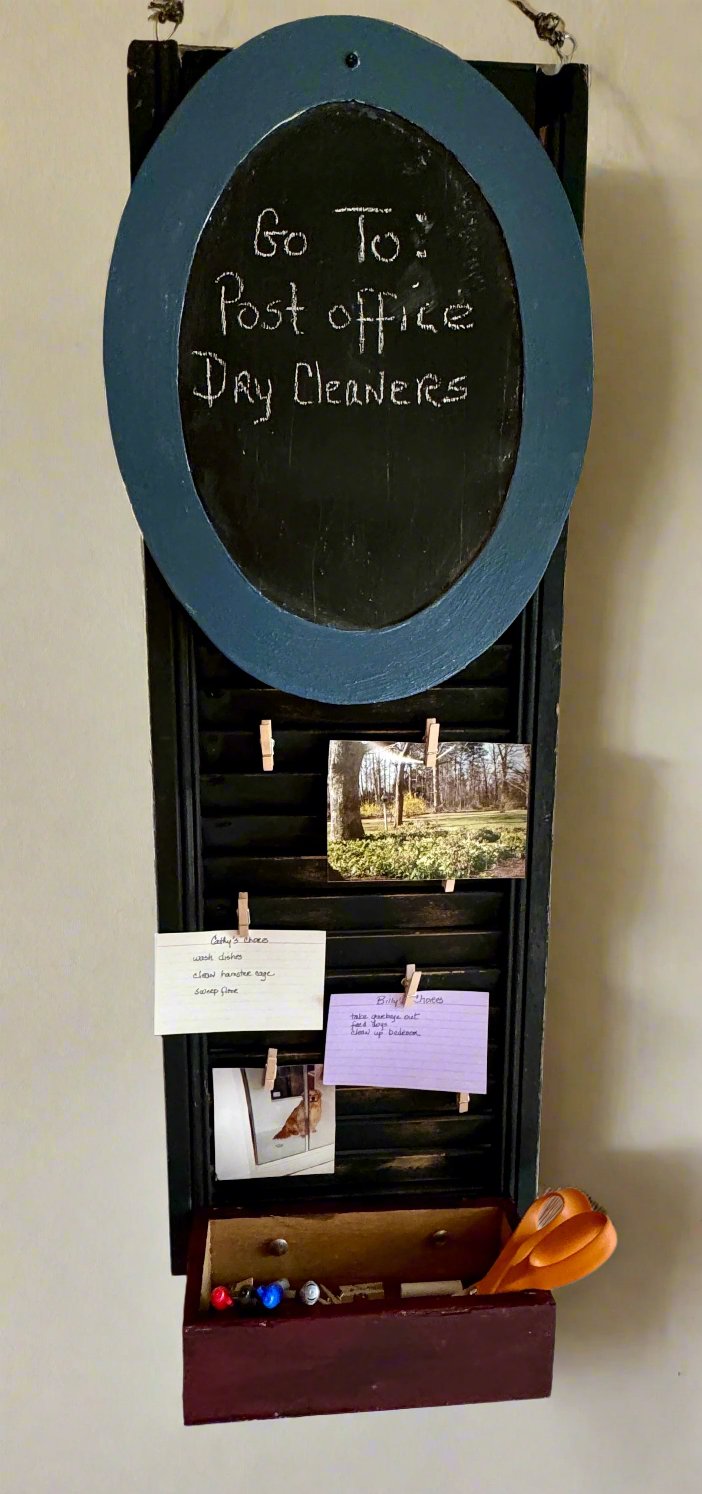 Old distressed black shutter with oval shaped chalkboard at top framed in a steel blue/gray color, wooden container painted rustic distressed red, mini-clothes pins for photos or reminders.  hangs on a wall.